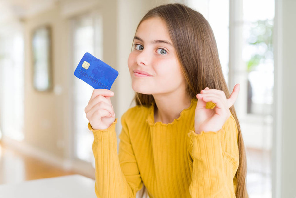 Menina bonita garoto segurando cartão de crédito muito feliz apontando com a mão e o dedo para o lado
 - Foto, Imagem
