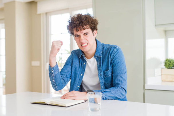 Young man reading a book at home annoyed and frustrated shouting with anger, crazy and yelling with raised hand, anger concept - Photo, Image