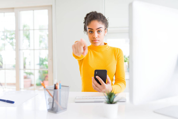 Молода афроамериканська дівчина, яка працює з комп'ютером і смартфоном, вказуючи пальцем на камеру і на вас, ручний знак, позитивний і упевнений жест з фронту. - Фото, зображення