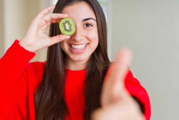 大きな笑顔で幸せな半分新鮮な緑のキウイを食べる美しい若い女性は、OKサインをやって、指で親指を上げ、優れた兆候 - 写真・画像