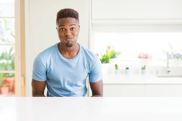 ハンサムなアフリカ系アメリカ人男性は、自宅でカジュアルなTシャツを着て、面白い顔で頬をふくらませます。空気で膨らんだ口、クレイジーな表情. - 写真・画像