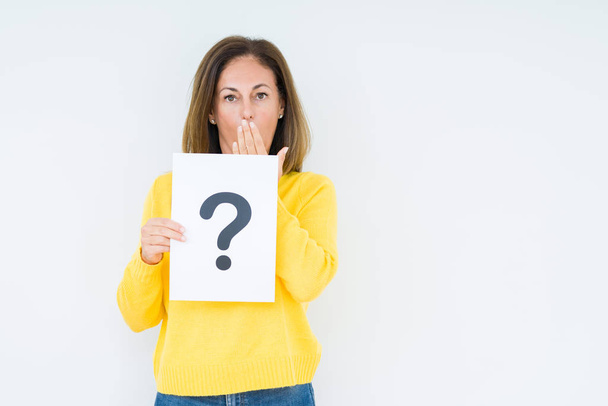 Middle age woman thinking and holding paper with question mark symbol over isolated background cover mouth with hand shocked with shame for mistake, expression of fear, scared in silence, secret concept - Fotografie, Obrázek