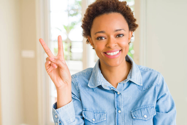 Young beautiful african american woman smiling with happy face winking at the camera doing victory sign. Number two. - Photo, Image