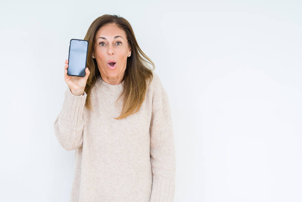 Izole arka plan üzerinde akıllı telefon ekranı gösteren orta yaşlı kadın sürpriz bir yüz ile şok korkmuş, korku ifade ile korkmuş ve heyecanlı - Fotoğraf, Görsel