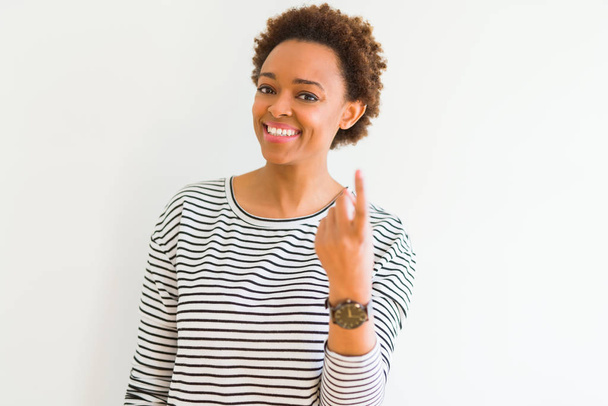 Jeune belle femme afro-américaine portant des rayures pull sur fond blanc Beckoning venir ici geste avec la main invitant heureux et souriant
 - Photo, image