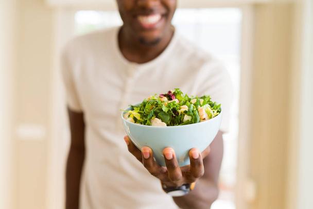 African young man holding a bowl of healthy salad smiling cheerf - Photo, Image