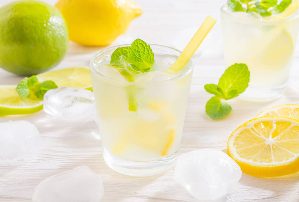Two glasses with summer drink mojito with lime, lemon and mint, with ice cubes on white wooden background. - Photo, image