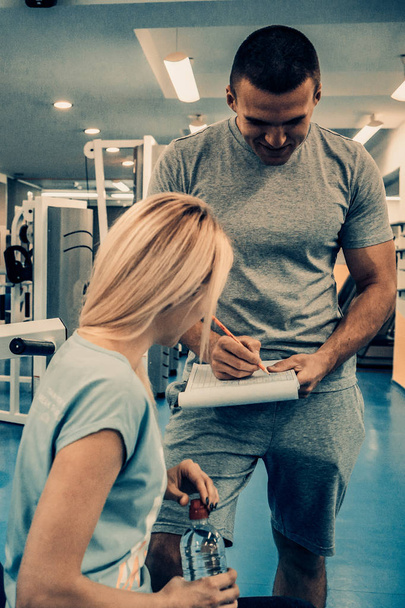 Vrouw en man in de sportschool, sportman schrijft notities voor training. - Foto, afbeelding