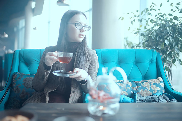 девушка в кафе пьет чай / современное кафе, молодая взрослая модель пьет чай и держит чашку в руке
 - Фото, изображение