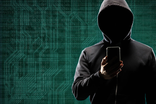Dangerous hacker with a smartphone gadget over digital background with binary code. Obscured dark face in mask and hood. Data thief, internet attack, darknet fraud, virtual reality and cyber security - Φωτογραφία, εικόνα