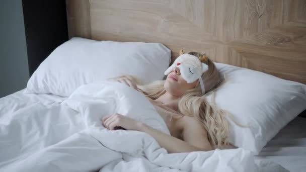 Νεαρή γυναίκα κοιμάται σε άνετο κρεβάτι με μάσκα για ύπνο. Δέστε τα μάτια σας. Πρωί στο δωμάτιο του ξενοδοχείου. Λευκό μαξιλάρι και κουβέρτα - Πλάνα, βίντεο