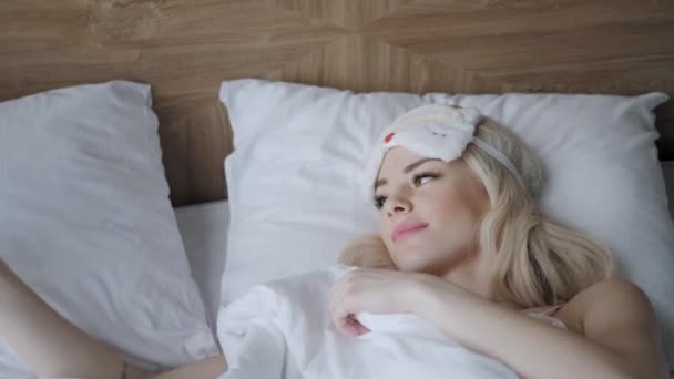Otel odasında sabah. Genç kadın rahat yatakta uyumak için maske yle uyur. Göz bağı. Beyaz yastık ve battaniye - Video, Çekim