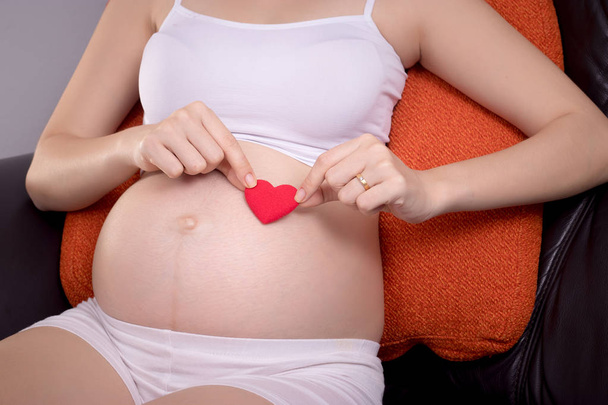 Glückliches Muttertagskonzept: Junge Schwangere halten ein Herz auf dem Bauch, anonymes Gesicht. schön asiatisch weiblich modell im sie 20s - Foto, Bild