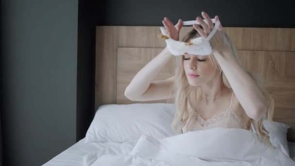 Frau bereitet sich auf den Schlaf vor und setzt eine Schlafmaske auf. Augenbinde. Morgen im Hotelzimmer. weißes Kissen und Decke - Filmmaterial, Video