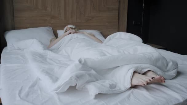 Genç bir kadın uyumak için rahat bir yatakta maske takar. Gözlerim bağlıydı. Otel odasında sabah oldu. Beyaz yastık ve battaniye - Video, Çekim