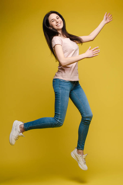 Cheerful brunette young woman in casual outlook jumping in mid air in studio. - Foto, afbeelding