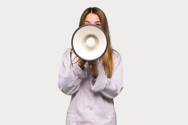Young doctor woman shouting through a megaphone to announce something on isolated grey background - Fotoğraf, Görsel