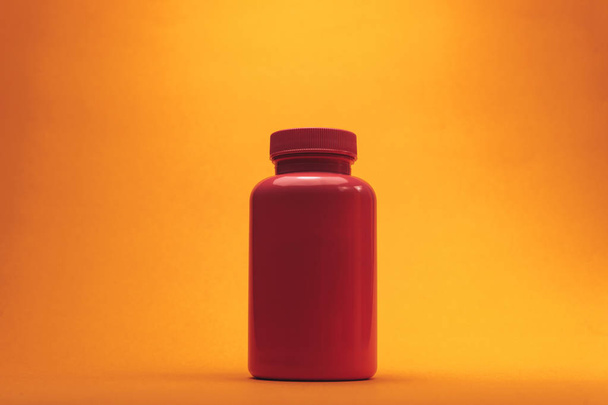 Roze fles voor pillen op een oranje achtergrond. - Foto, afbeelding