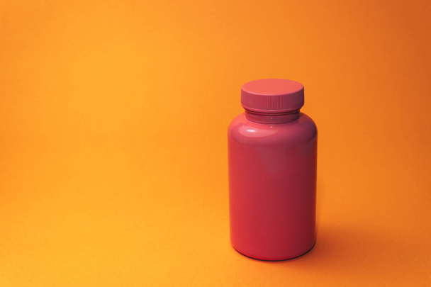 Рожева пляшка для таблеток на помаранчевому фоні
. - Фото, зображення