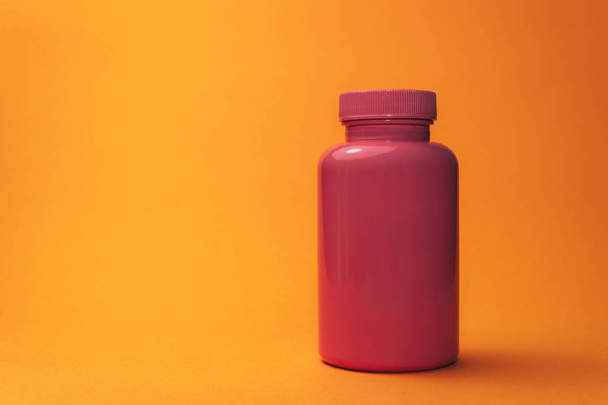 オレンジ色の背景に錠剤のためのピンクのボトル. - 写真・画像