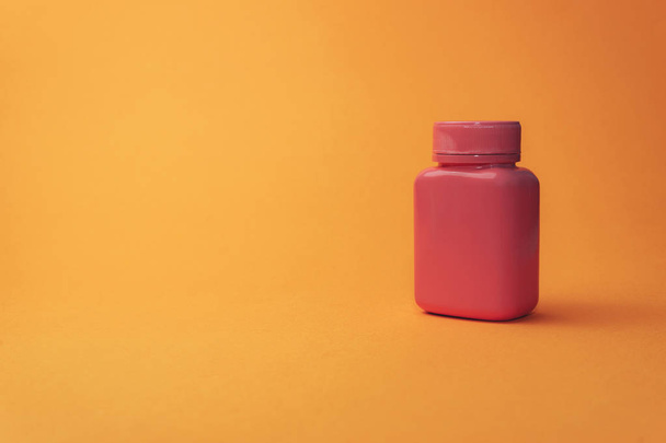 オレンジ色の背景に錠剤のためのピンクのボトル. - 写真・画像