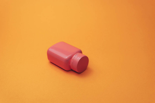 rosafarbene Flasche für Pillen auf orangefarbenem Hintergrund. - Foto, Bild