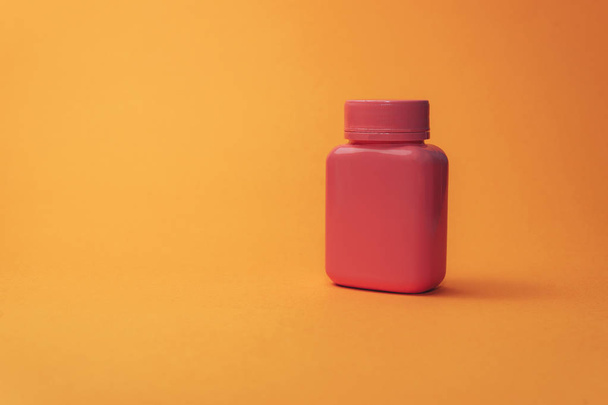 Pink bottle for pills on a orange background. - Photo, Image