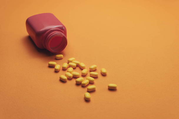 Beautiful pink bottle and yellow pills on a orange background. Top view. - Fotografie, Obrázek