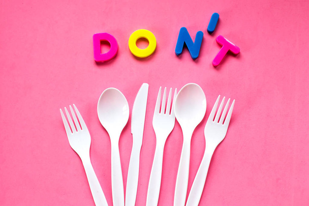 Flat lay of plastic white cutlery on pink background. Recycling concept. - Фото, изображение
