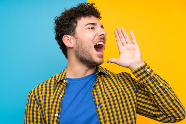 Man with curly hair over colorful wall shouting with mouth wide open - Photo, image