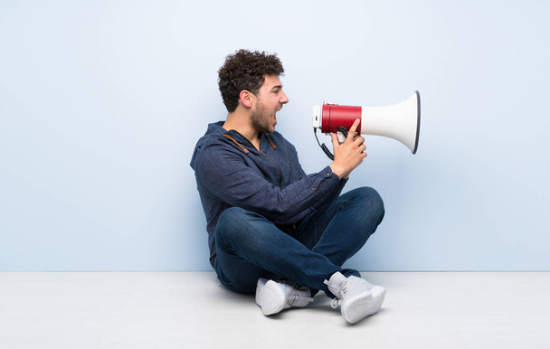 Young man sitting on the floor shouting through a megaphone - Foto, imagen