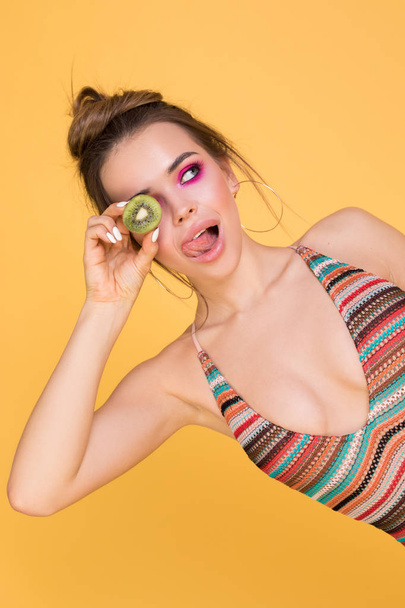 Girl in a swimsuit holding a kiwi near his eyes. - Foto, afbeelding
