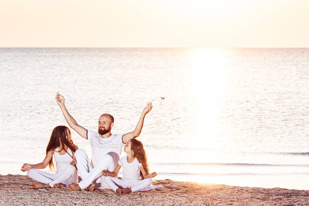 familie bij Dawn doen yoga of meditatie op het strand. - Foto, afbeelding