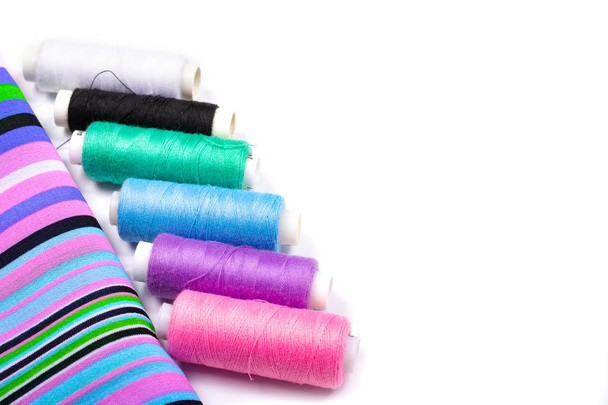 Sewing. Background of striped fabric and spools of threads of different colors on a white background. Side view, space for text, Copy space, - Photo, Image