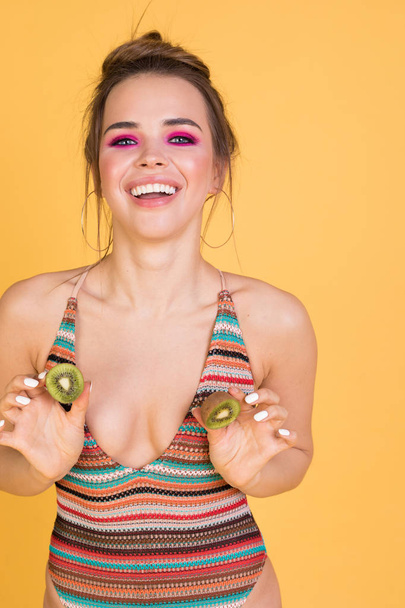 Funny girl in a swimsuit holding a kiwi at the chest. - Fotó, kép