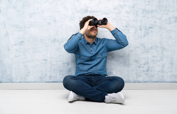Young man sitting on the floor with black binoculars - Photo, Image