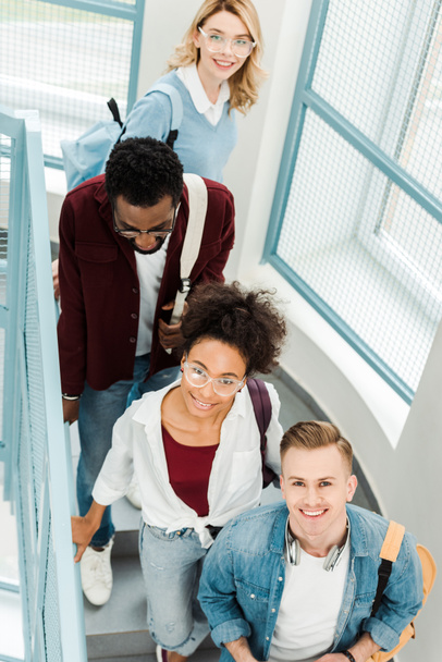 vista aérea de cuatro estudiantes multiétnicos sonrientes con mochilas en las escaleras
 - Foto, Imagen
