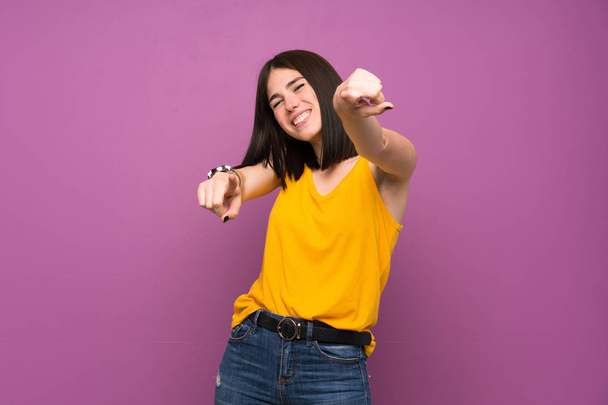 Nuori nainen yli eristetty violetti seinä osoittaa sormella sinua hymyillen
 - Valokuva, kuva