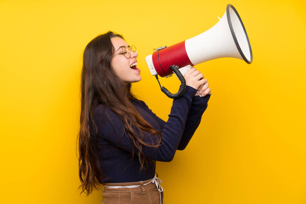 Девочка-подросток над изолированной желтой стеной кричит через мегафон
 - Фото, изображение
