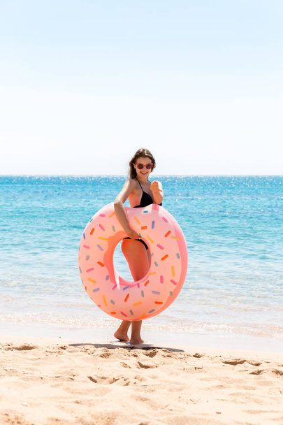 glückliches Weibchen am Strand, das mit einem aufblasbaren Donut-Ring spielt. Sommerferien und Urlaubskonzept - Foto, Bild
