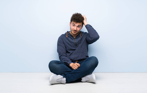 Молодий чоловік сидить на підлозі з виразом розчарування і не розуміння
 - Фото, зображення
