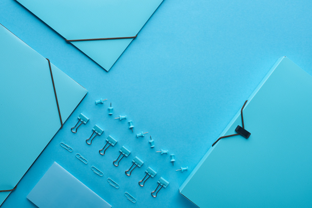 colocação plana de pastas de papel e vários artigos de papelaria isolados em azul
  - Foto, Imagem