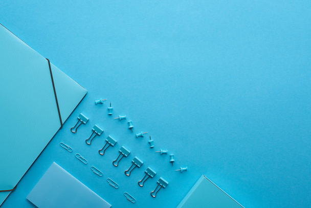 Плоская бумажная переплетка и различные канцелярские принадлежности, изолированные на голубом с копировальным пространством
 - Фото, изображение