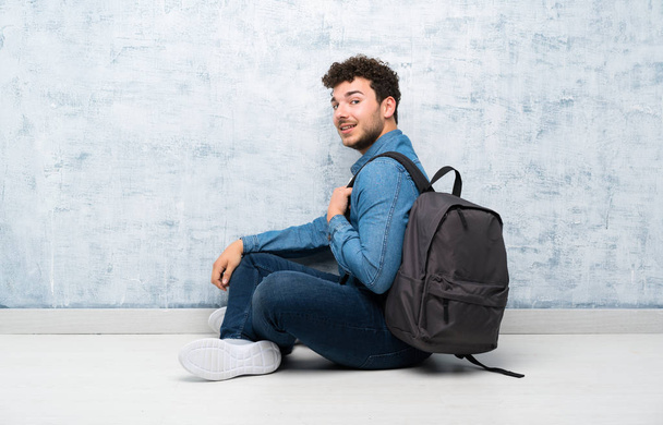 Young man sitting on the floor with backpack - Foto, afbeelding