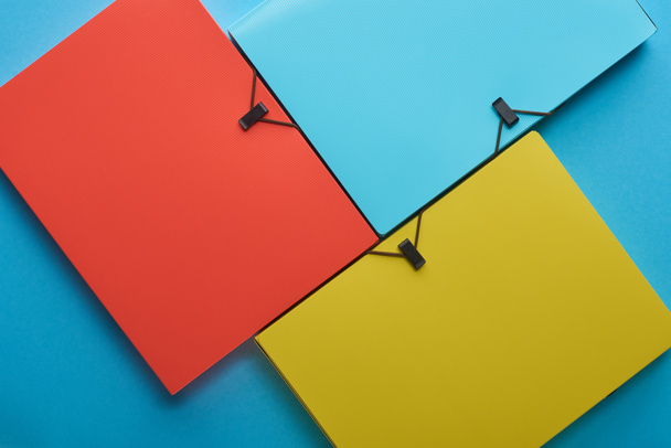 верхний вид рассортированных разноцветных бумажных папок на голубом
 - Фото, изображение