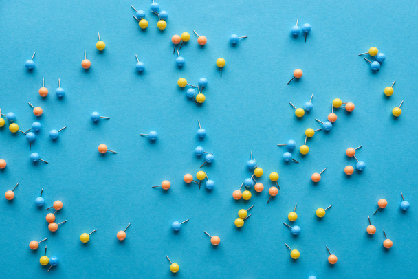 Κορυφαία όψη των πολύχρωμων διάσπαρτων καρφίτσες Push που απομονώνονται σε μπλε - Φωτογραφία, εικόνα