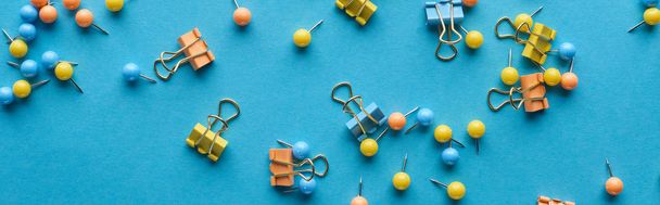 panoramic shot of colorful scattered push pins and paper clips isolated on blue - Foto, Imagen