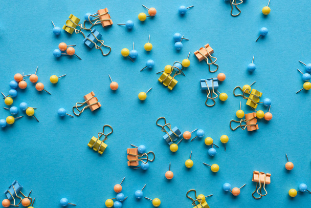 top view of colorful scattered push pins and paper clips isolated on blue - Фото, изображение
