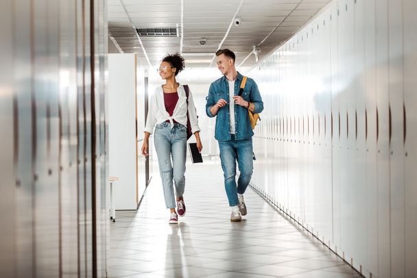 full length view of two multiethnic students in corridor in university - Photo, Image