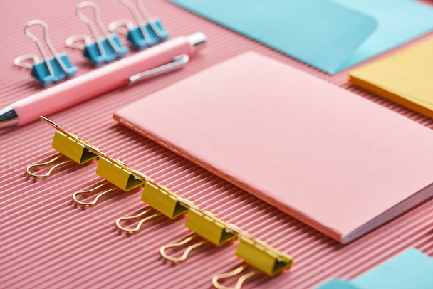 блокнот, паперові затискачі та різнокольорові канцелярські товари на рожевому
  - Фото, зображення